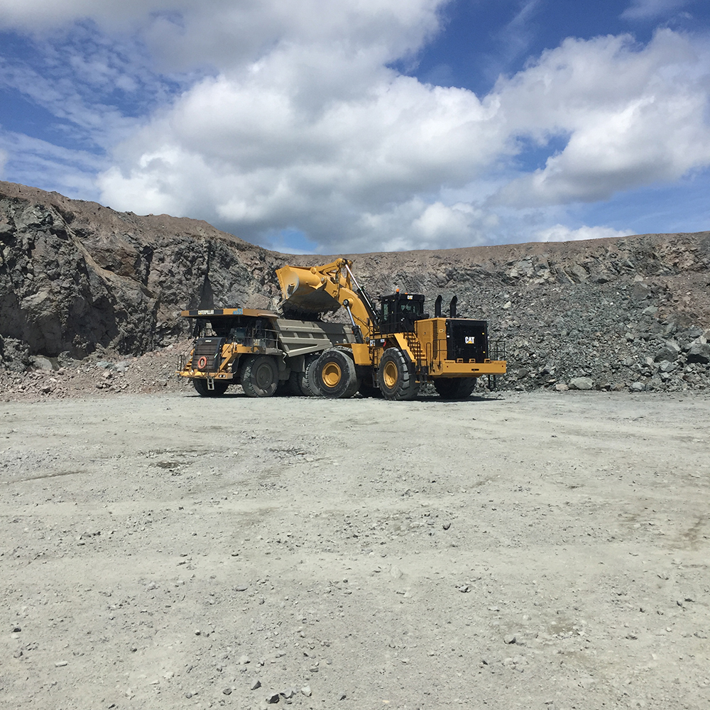 Large wheel loader filling a quarry haul truck beneath a bright open sky