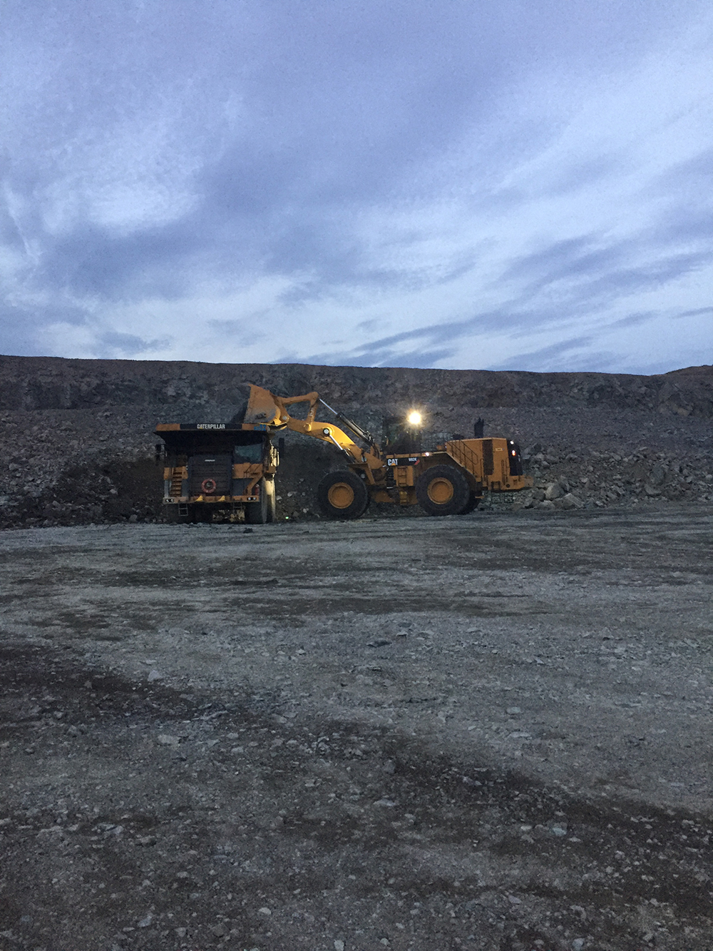 Wheel loader loading a quarry truck at dusk with its work lights on