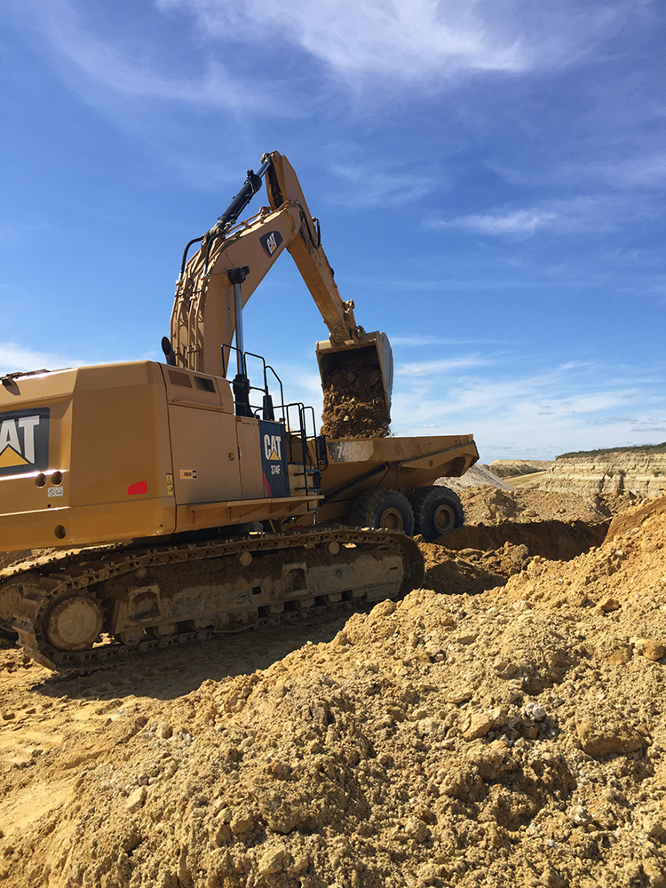 Excavator loading an articulated dump truck in a broad active earthwork excavation