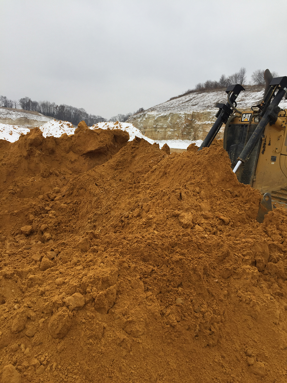 Excavator and haul trucks moving material through a snow-covered excavation