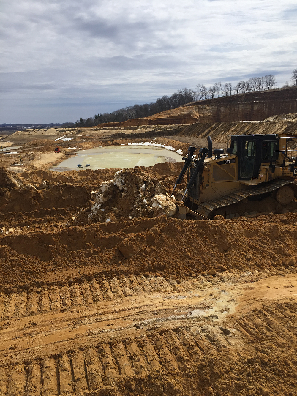Dozer working beside an excavated basin with layered cuts in the distance