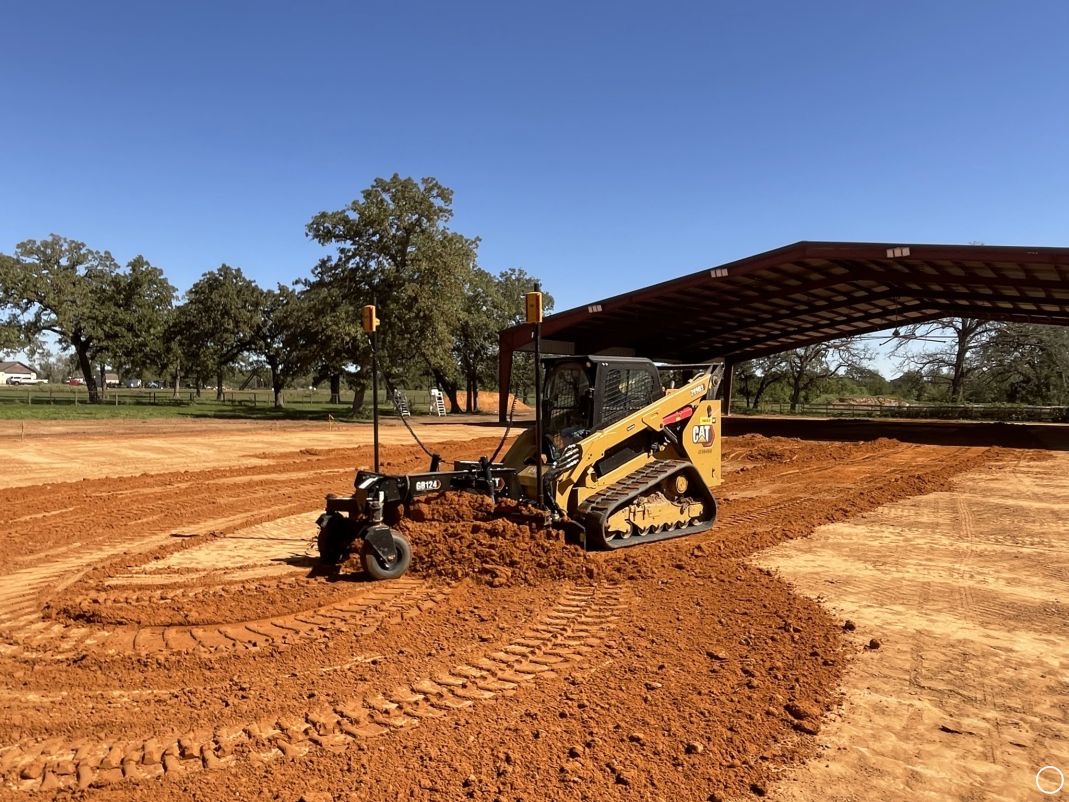 Tracked skid steer grading soil beside an active steel-frame construction site